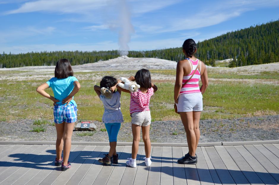 A family watches the Old Faithful geyser eruption in Yellowstone National Park during summer.