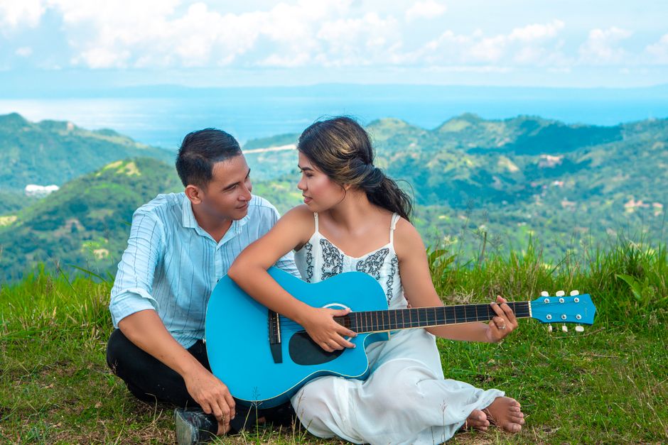 A couple sharing romantic moments with a guitar amidst breathtaking mountain scenery.