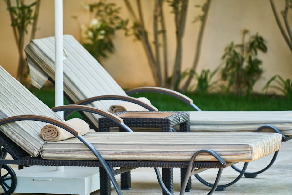 Elegant wooden sun loungers lined up poolside at a tropical resort, perfect for relaxation.