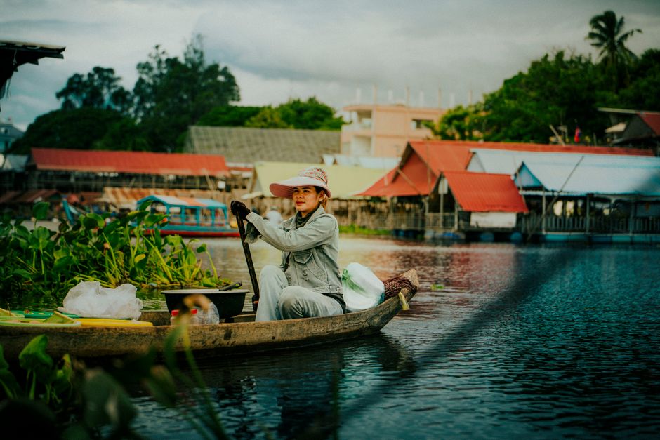 A Cambodian woman paddles through a picturesque village setting, showcasing traditional life on the water.
