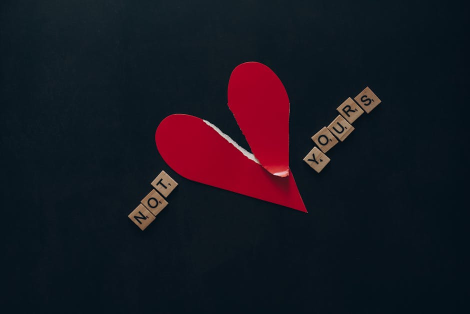 Conceptual image of a torn red heart with Scrabble tiles spelling 'NOT YOURS' on a dark background.