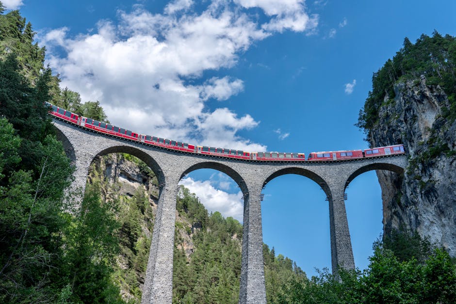 Red train crosses the iconic Landwasser Viaduct in Switzerland, surrounded by stunning alpine scenery.