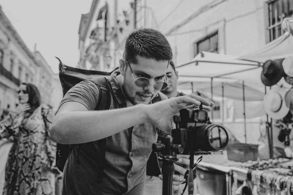Black and white portrait of a street photographer adjusting his camera in an outdoor market setting.