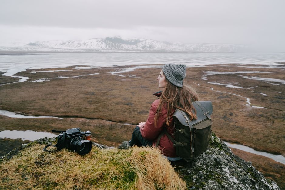 Woman with backpack and camera sitting on a cliff, viewing misty mountains.
