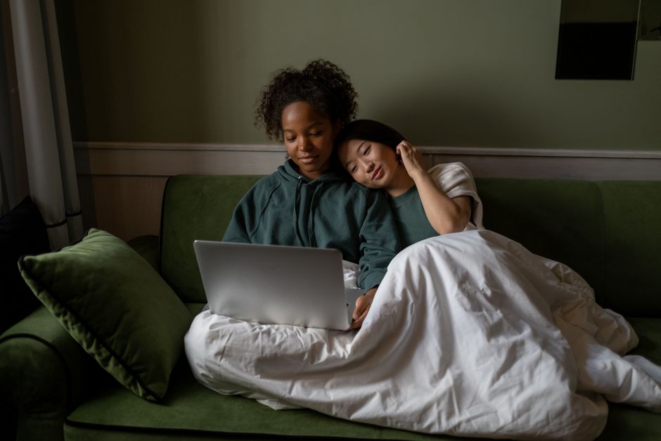 Two women enjoying a cozy moment on a couch with a laptop, embracing love and technology.
