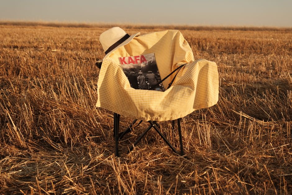A yellow-checkered chair with a hat and magazine in a serene rural field setting.