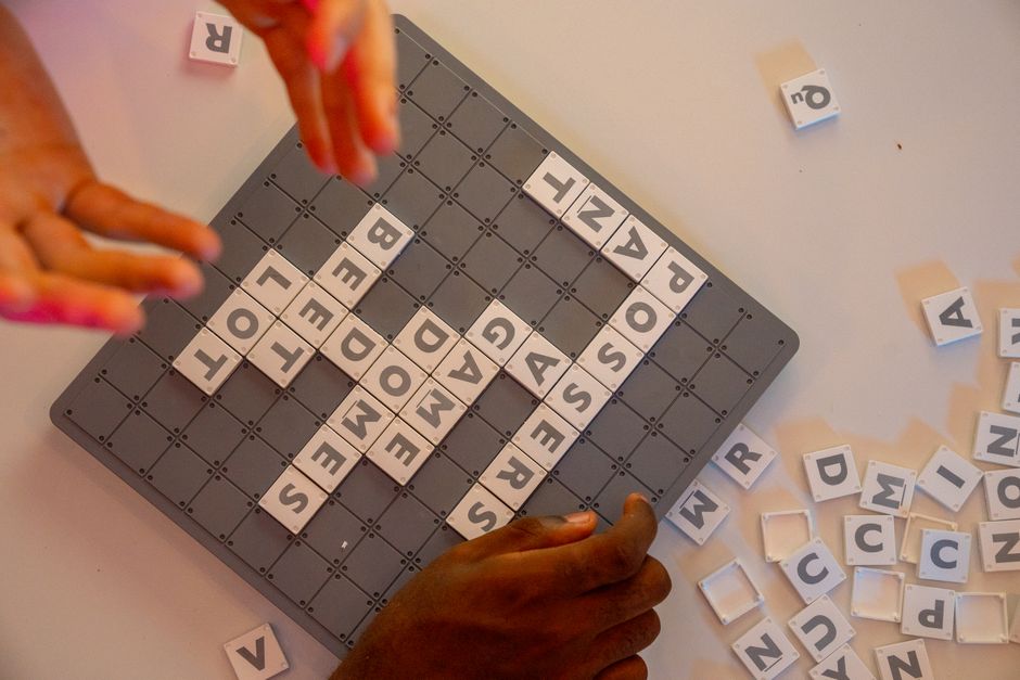 Hands arranging letter tiles on a game board, creating words, fostering connection.
