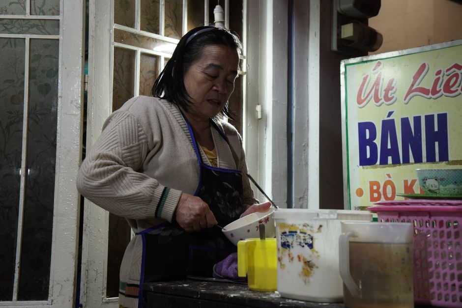 A woman preparing Vietnamese banh dish at a street vendor stall during the night.