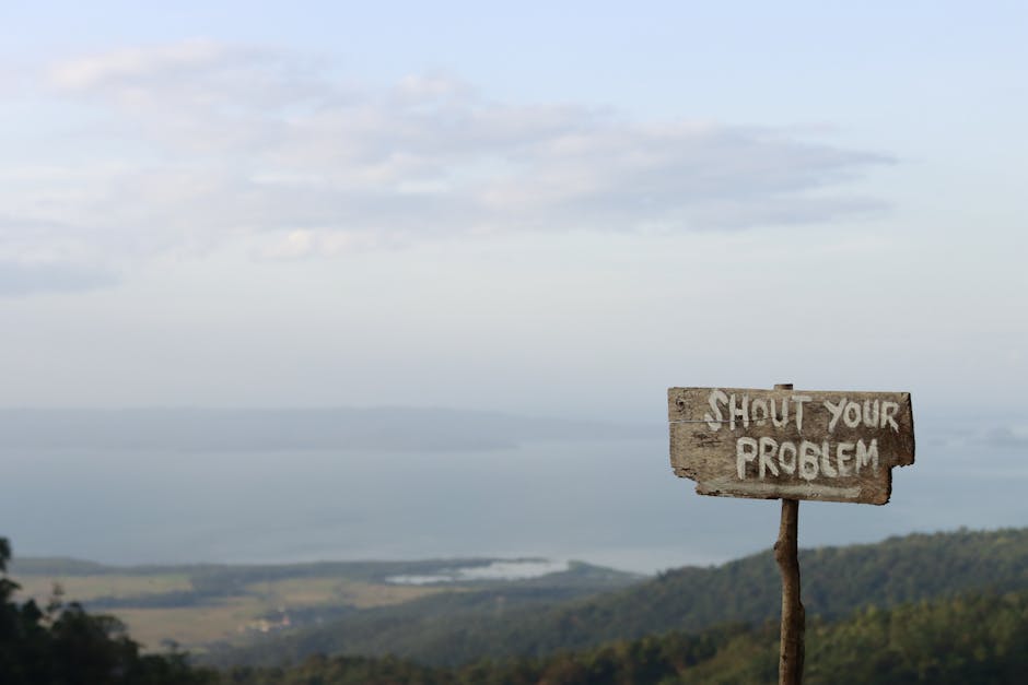 Wooden sign inscribed with 'Shout Your Problem' facing a beautiful mountain landscape under a blue sky.