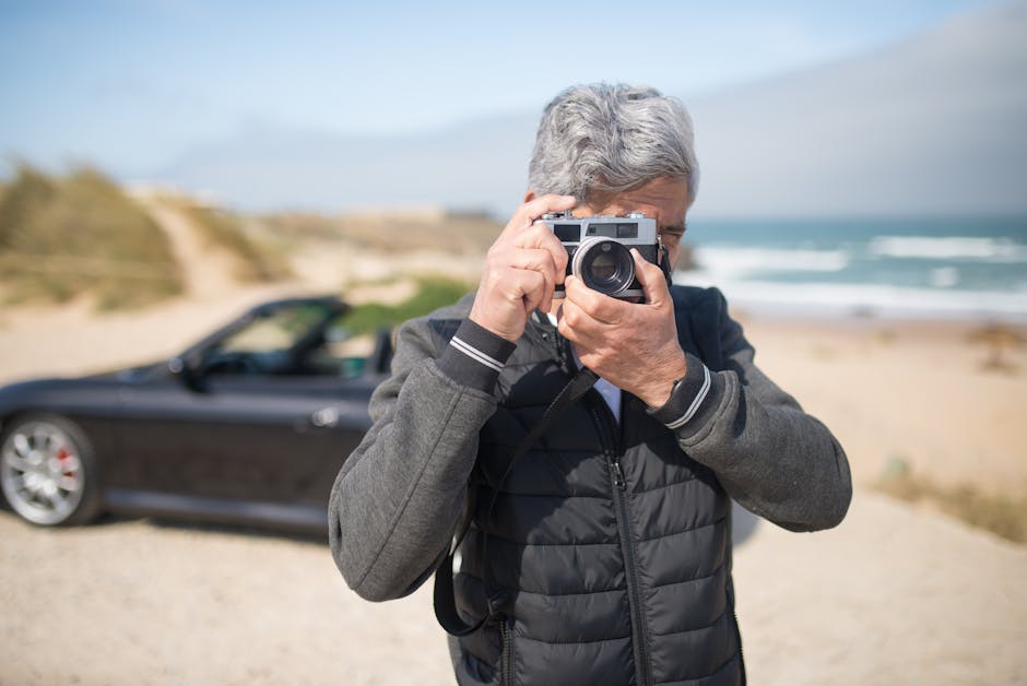 Senior man taking pictures by a scenic beach in Portugal with a vintage camera.